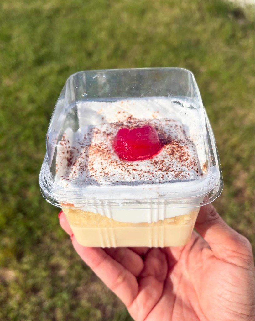 Bachata Bakery classic tres leches cake cup topped with whipped cream, cinnamon, and a cherry